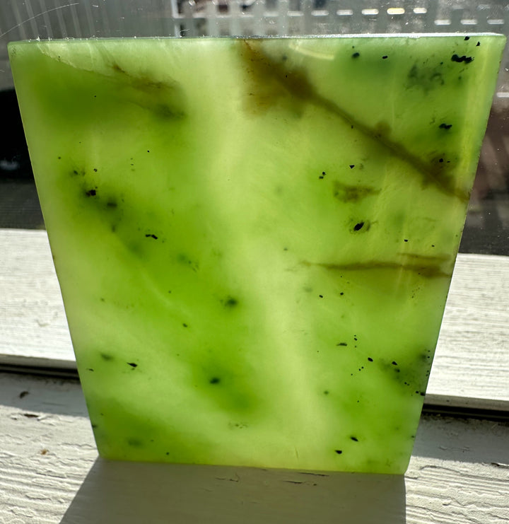 155-gram neon green nephrite jade slab with dark inclusions viewed at a slight angle