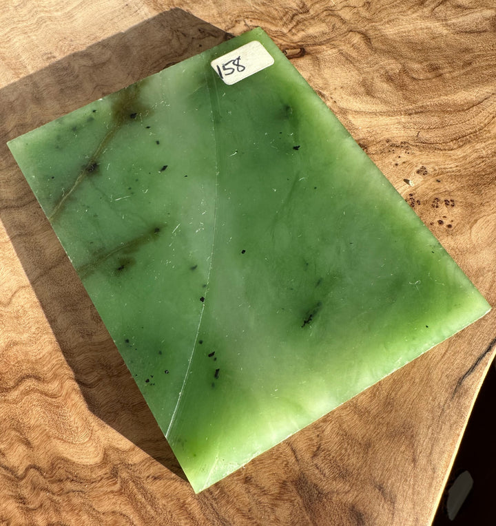 Siberian nephrite jade slab in vivid green with black specks on a wooden surface labeled 158