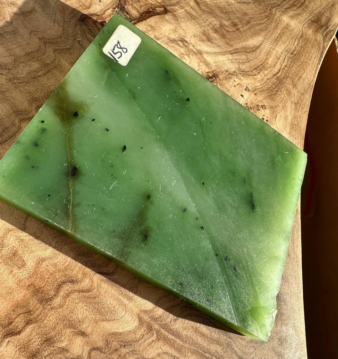 Siberian nephrite jade slab on a wood surface with light and dark green tones and a small corner sticker.