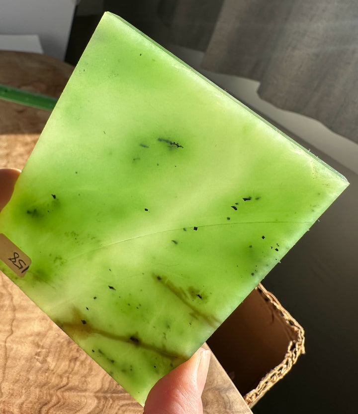 Bright lime green nephrite jade slab held in hand with scattered dark specks.