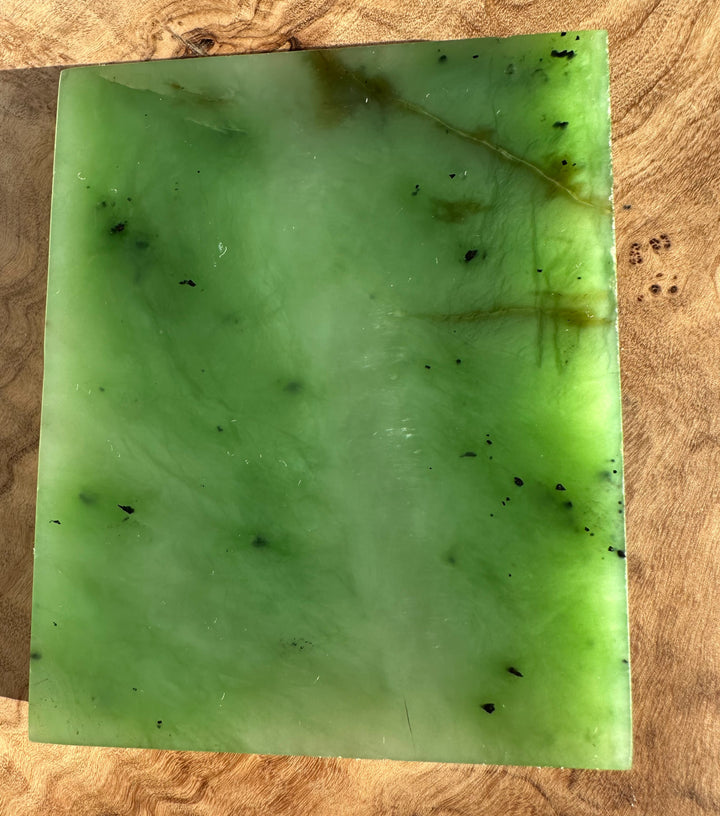 Siberian Nephrite Jade Slab in vibrant green with darker flecks on a wooden surface