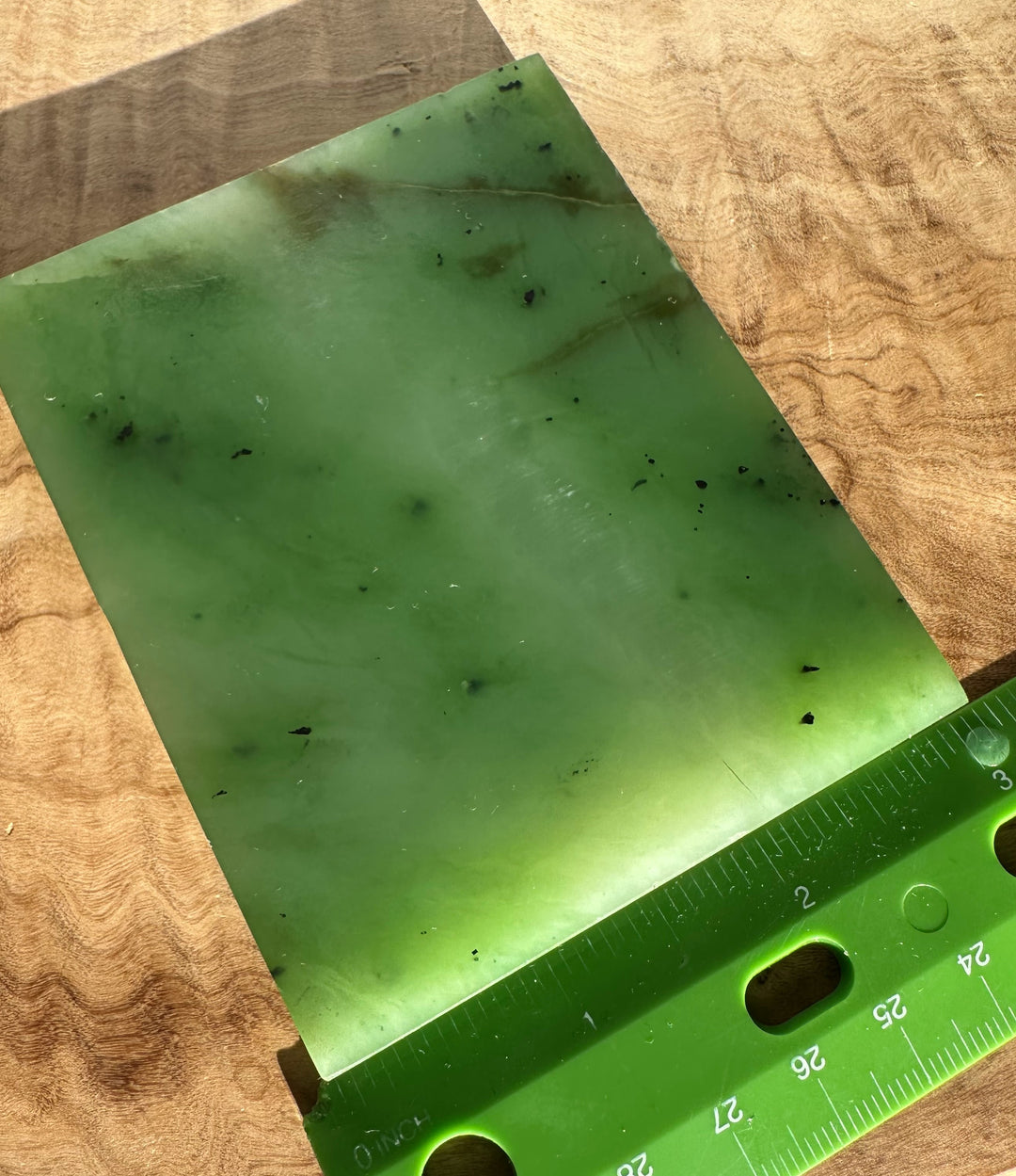 Pale green Siberian nephrite jade slab on wood with faint veins and a ruler for scale.