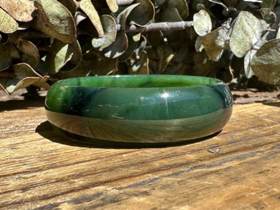 A Grade Canadian Nephrite Jade Bangle 53.5x16.8mm featuring a chatoyant band on a wooden surface