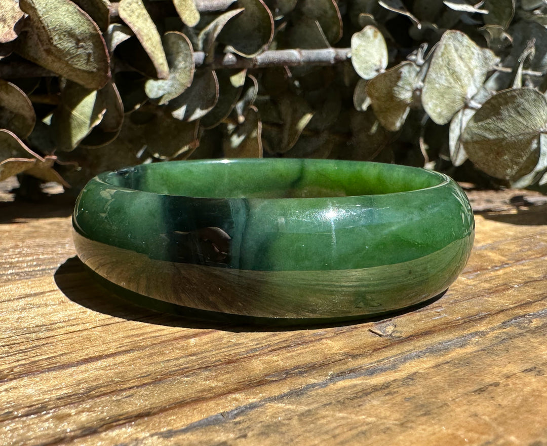 Green nephrite jade bangle with a chatoyant band and reflective highlights on sunlit wood