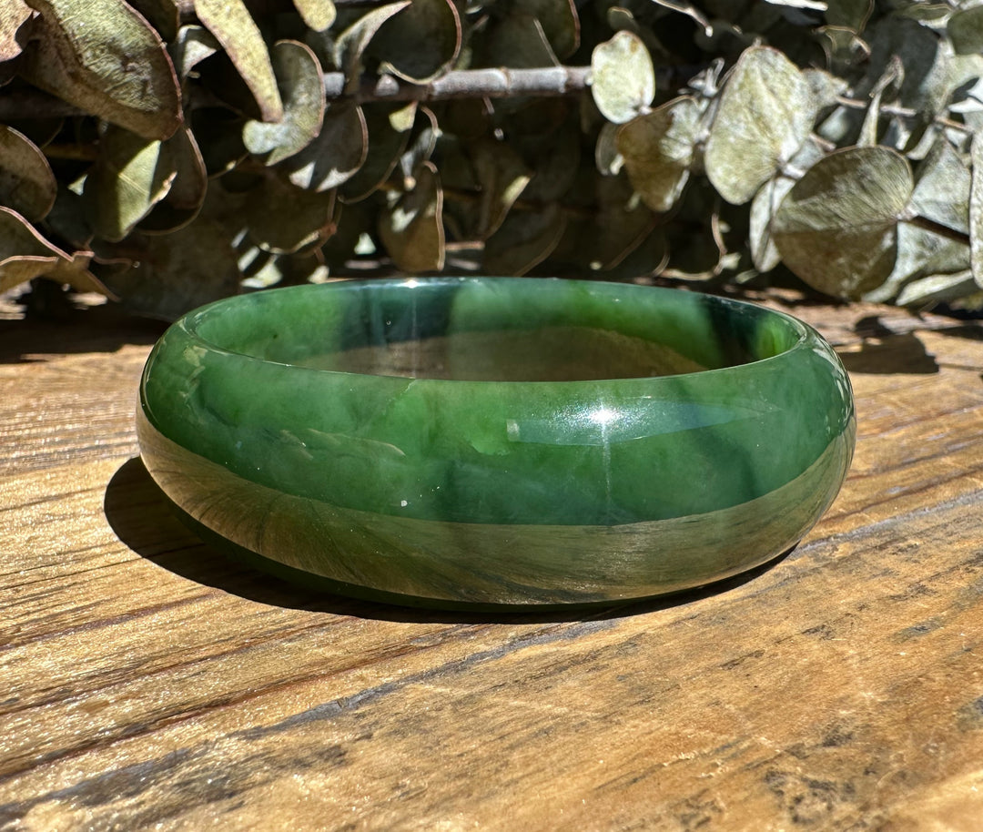 A Grade Canadian nephrite jade bangle featuring a chatoyant band on weathered wood
