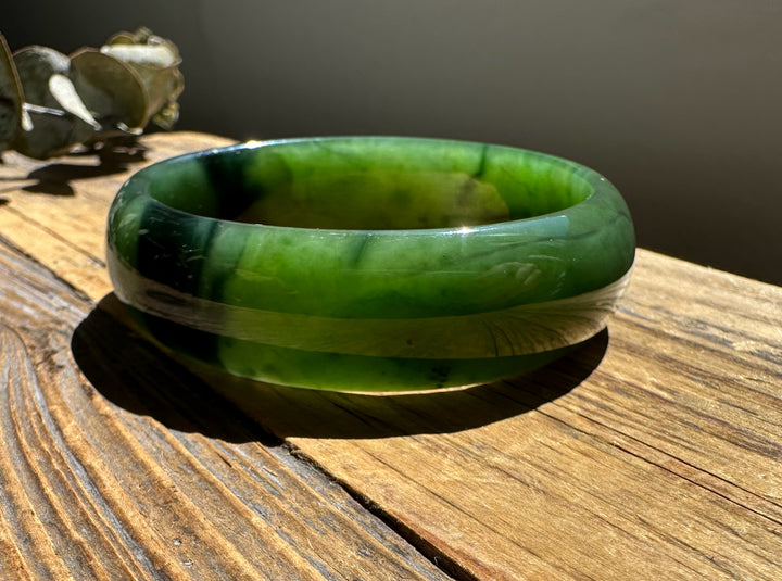 A Grade Canadian nephrite jade bangle with a chatoyant band on a sunlit wooden surface
