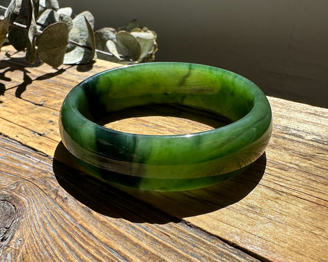 A Grade Canadian nephrite jade bangle showing vivid green tones and a chatoyant band on sunlit wood
