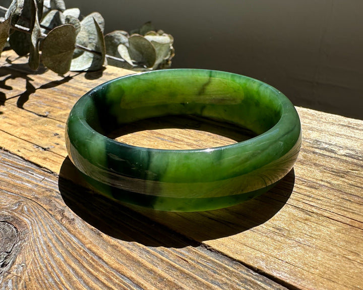 A Grade Canadian nephrite jade bangle showing vivid green tones and a chatoyant band on sunlit wood