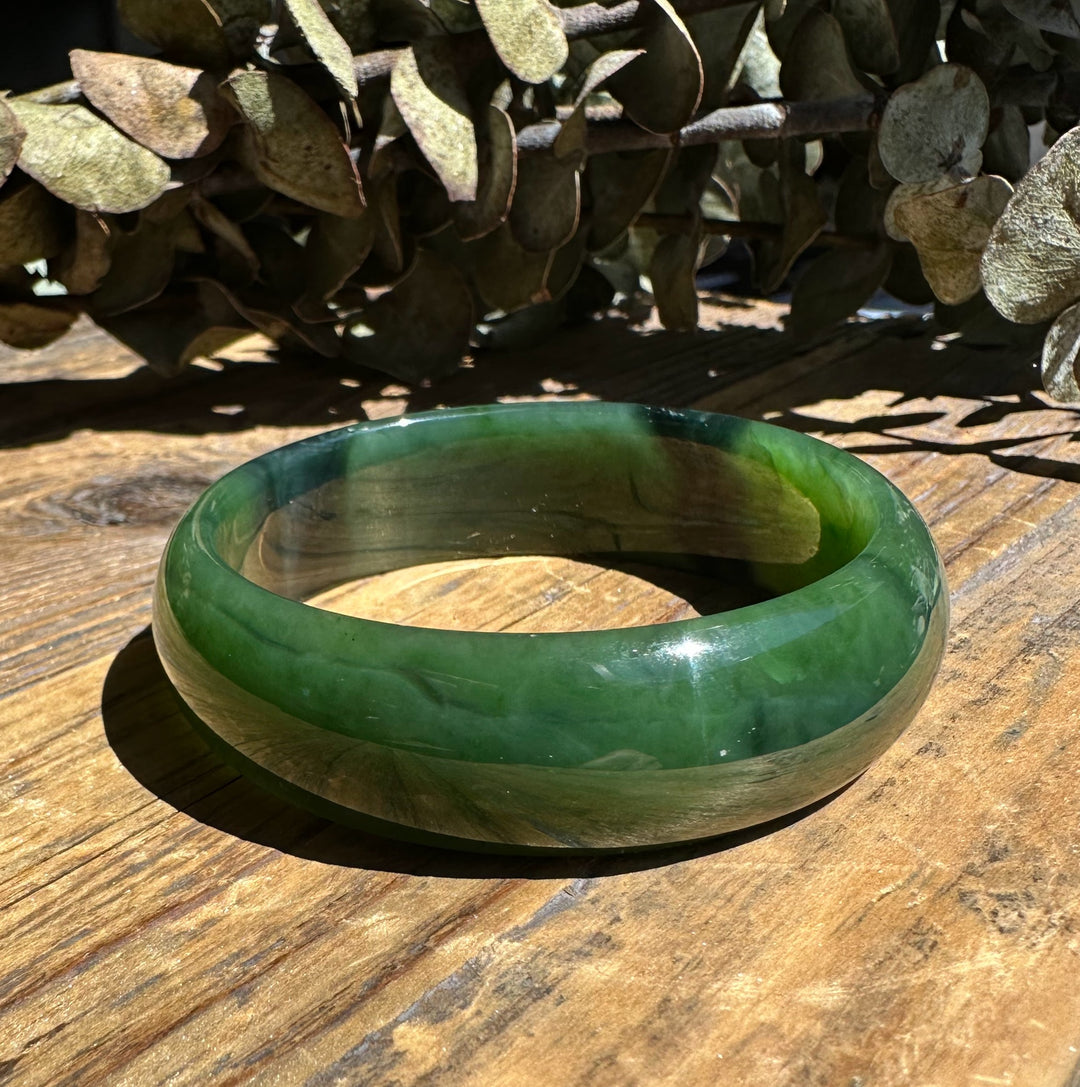 A grade Canadian nephrite jade bangle with a chatoyant band resting on a wooden surface
