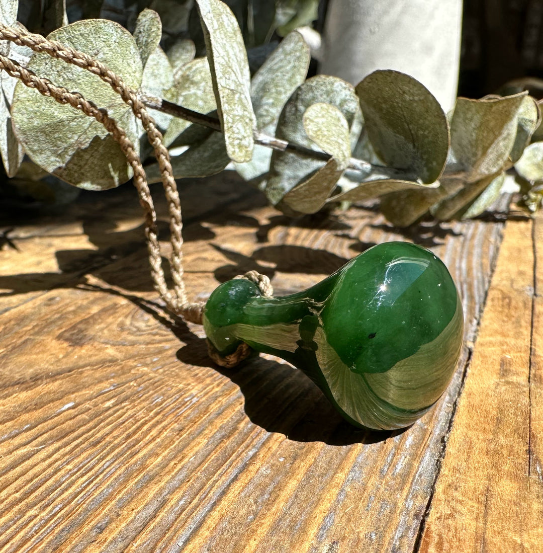 Green Poi Pounder pendant resting on weathered wood with sage leaves in the background