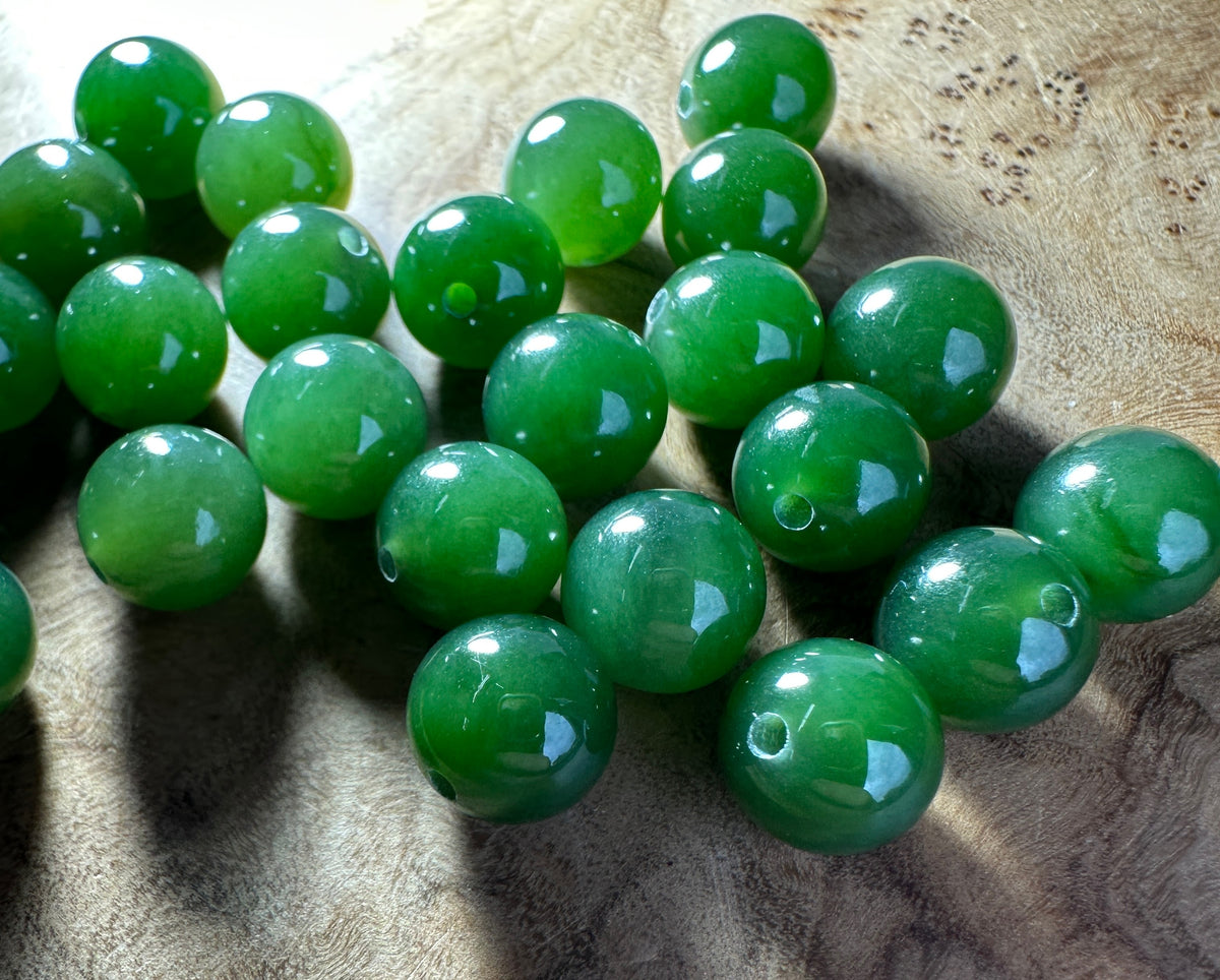 Dark green Canadian jade beads with bright light hitting them. On a wooden surface