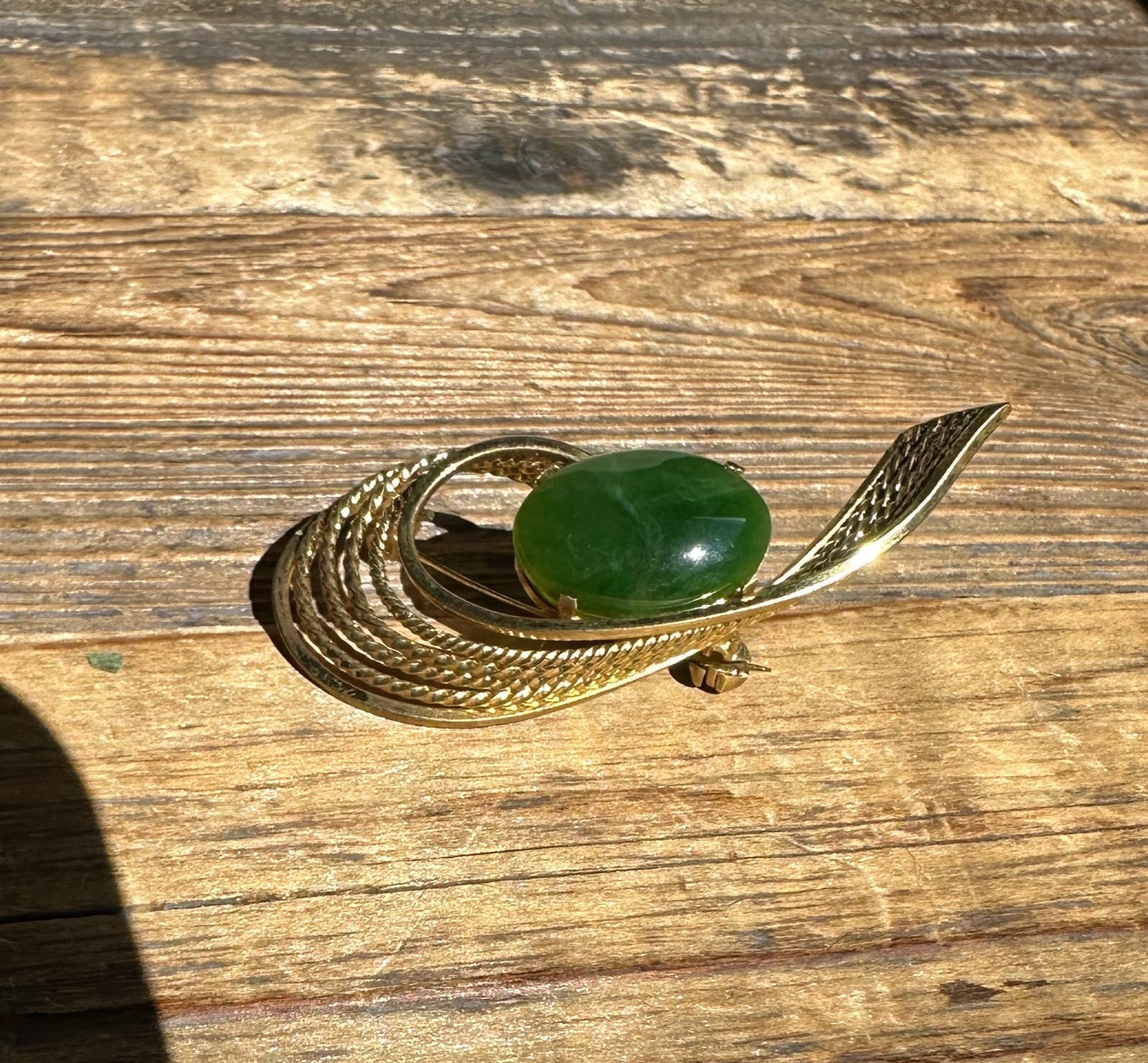 Top view of a gold vintage brooch showcasing a green jade cabochon encircled by braided rope bands.