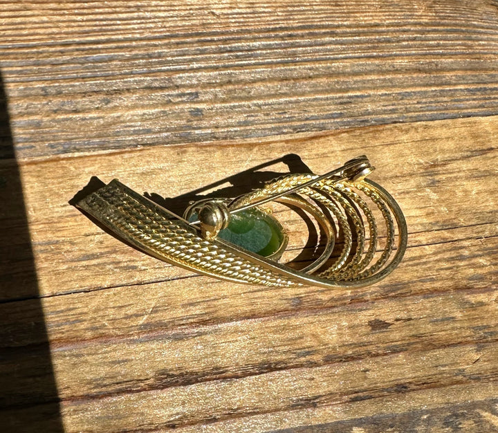 Vintage Canadian Jade Brooch in gold with a green jade cabochon and textured curved bands on wood