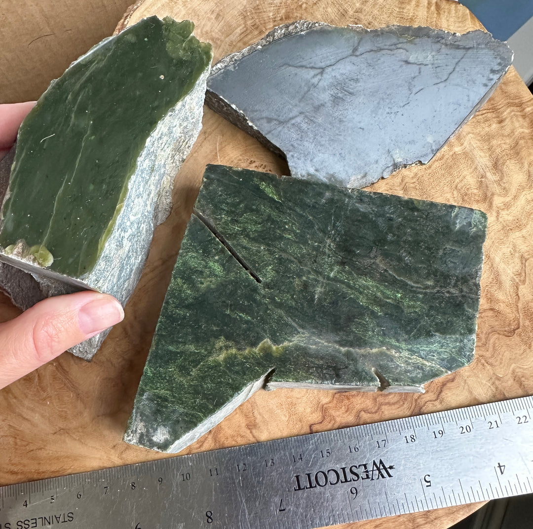 3 pieces of green Canadian nephrite jade beside a ruler on a wooden base