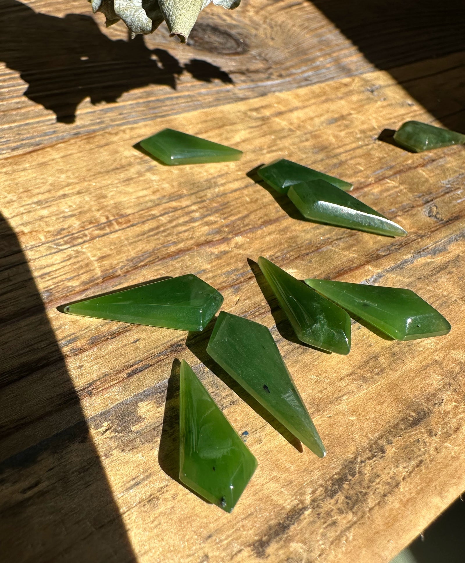 Green nephrite jade kite shaped beads 10/20mm arranged on a sunlit wooden surface.