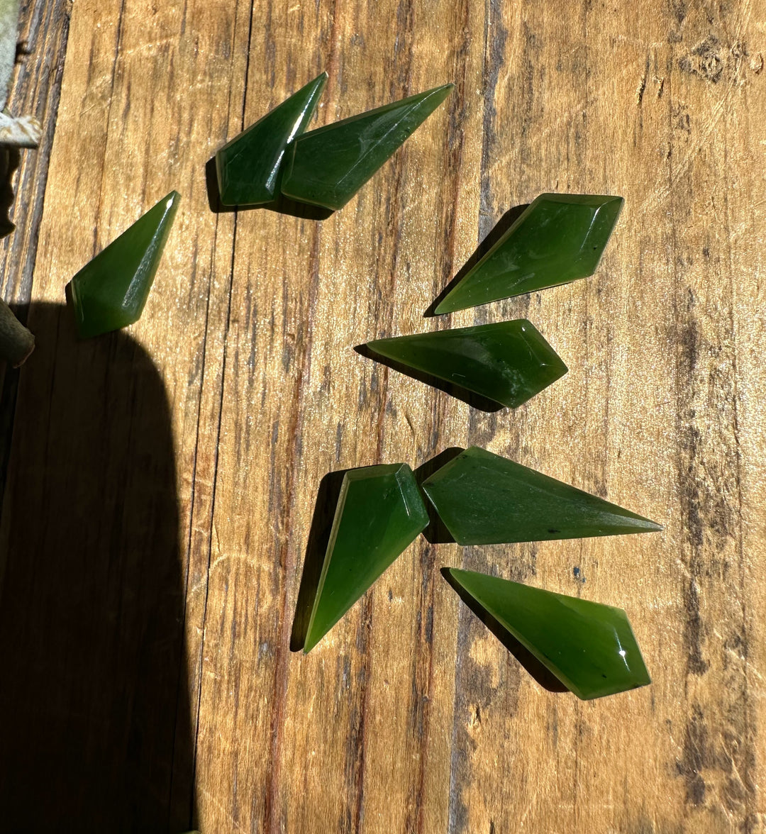 Polished green nephrite jade kite shaped pieces 10/20mm on a wooden surface.