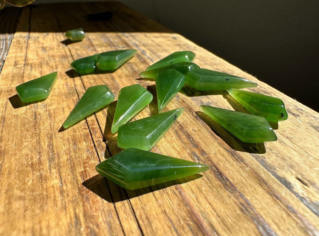 Green nephrite jade kite shaped beads 10/20mm scattered on a sunlit wooden surface.