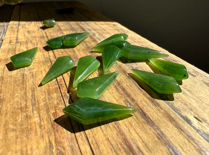 Green nephrite jade kite shaped beads 10/20mm scattered on a sunlit wooden surface.
