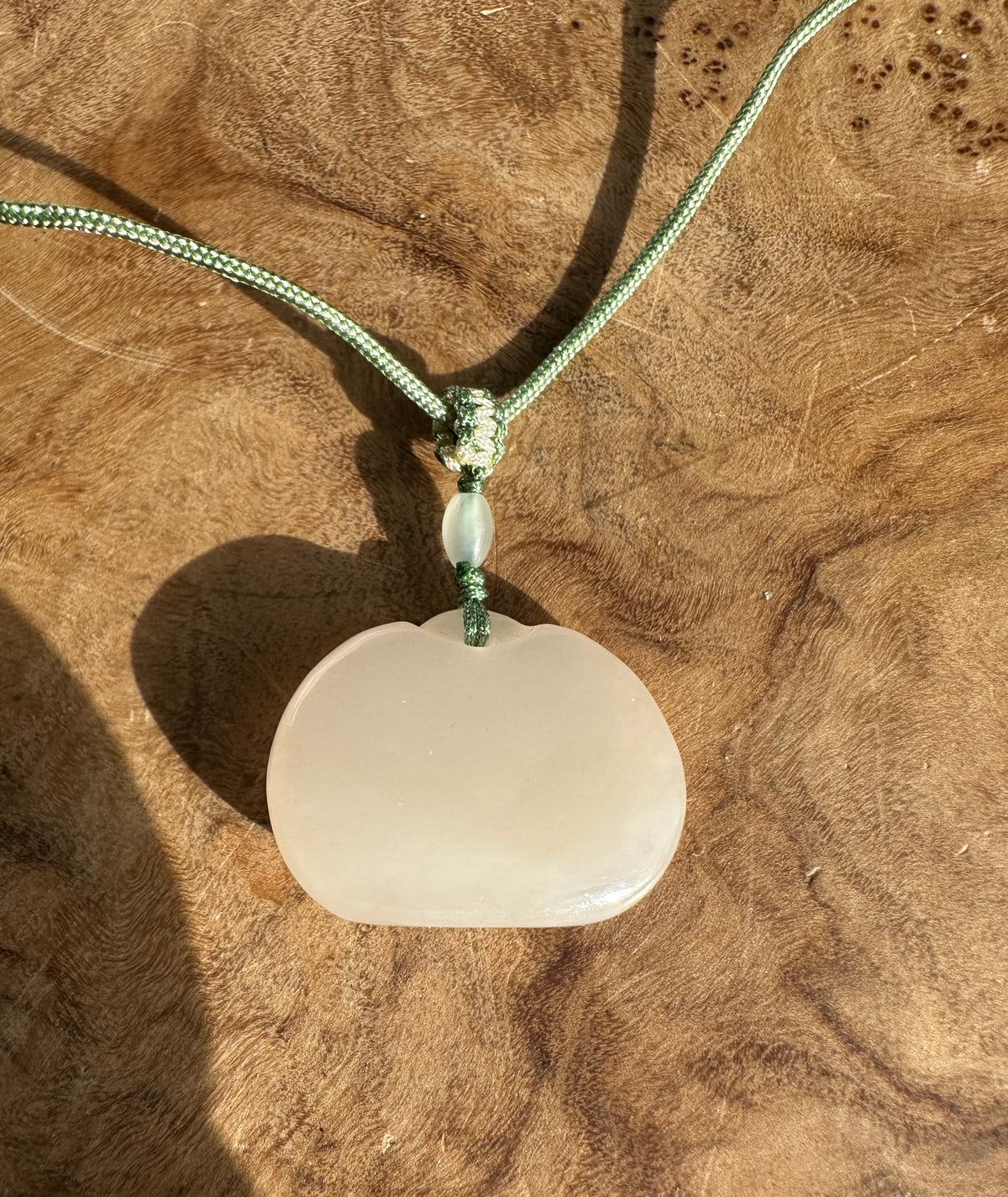 Dainty white nephrite jade Ruyi pendant suspended on green cord with a small pale green bead above the disk.