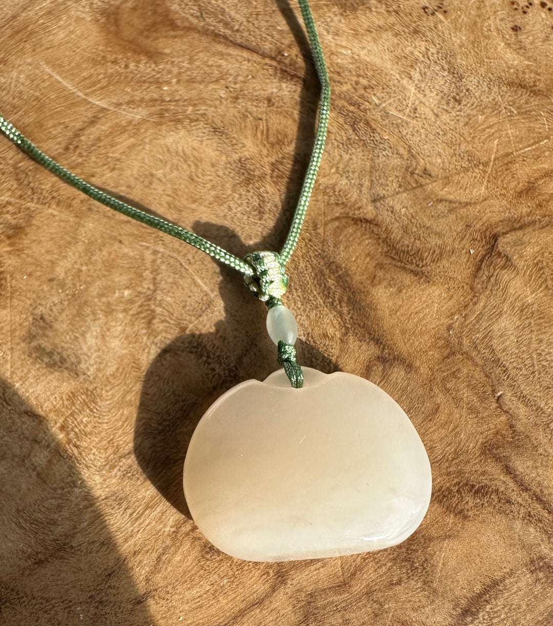 Dainty white nephrite jade Ruyi pendant with green cord knot and bead against a wooden background.