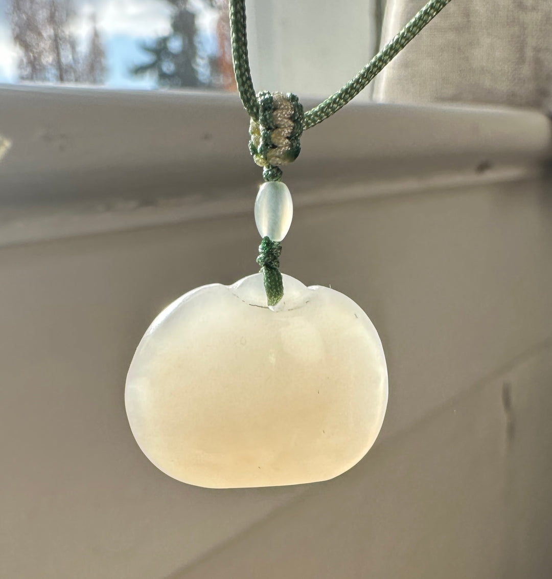 Dainty white nephrite jade Ruyi pendant on a green braided cord tied in a knot against a blurred background.