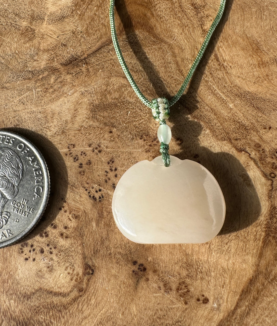 Dainty white nephrite jade Ruyi pendant on a green braided necklace with a knot and a coin for scale on wood.