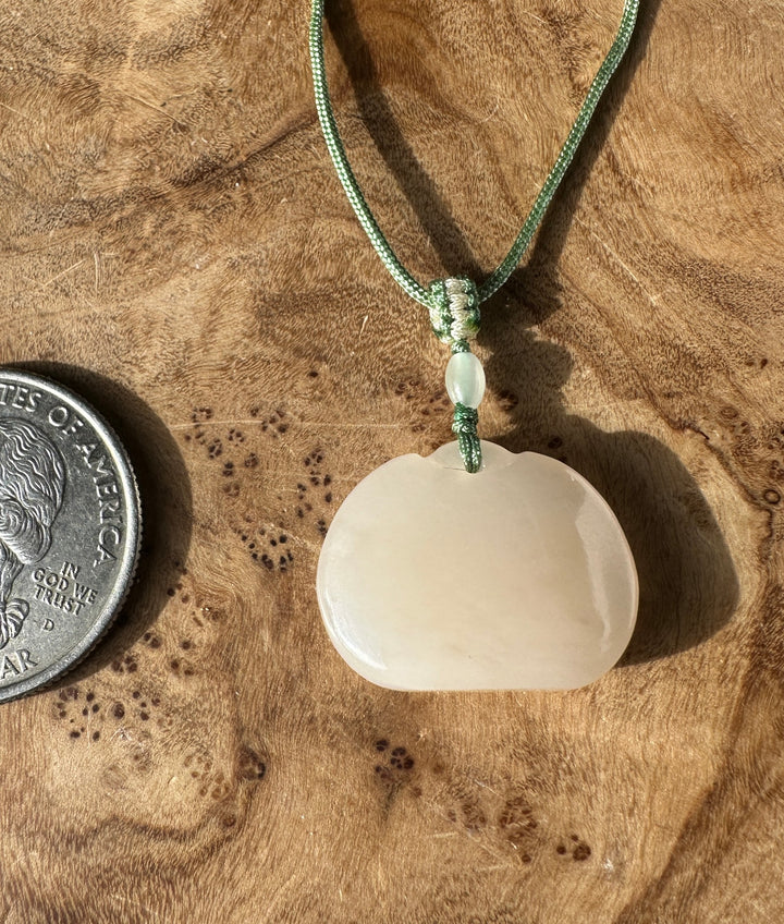 Dainty white nephrite jade Ruyi pendant on a green braided necklace with a knot and a coin for scale on wood.