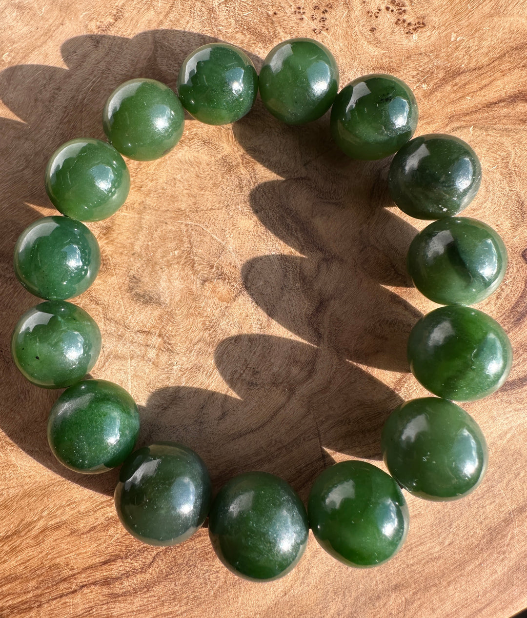 Top view of 14mm Canadian nephrite jade beads forming a circular bracelet on wood