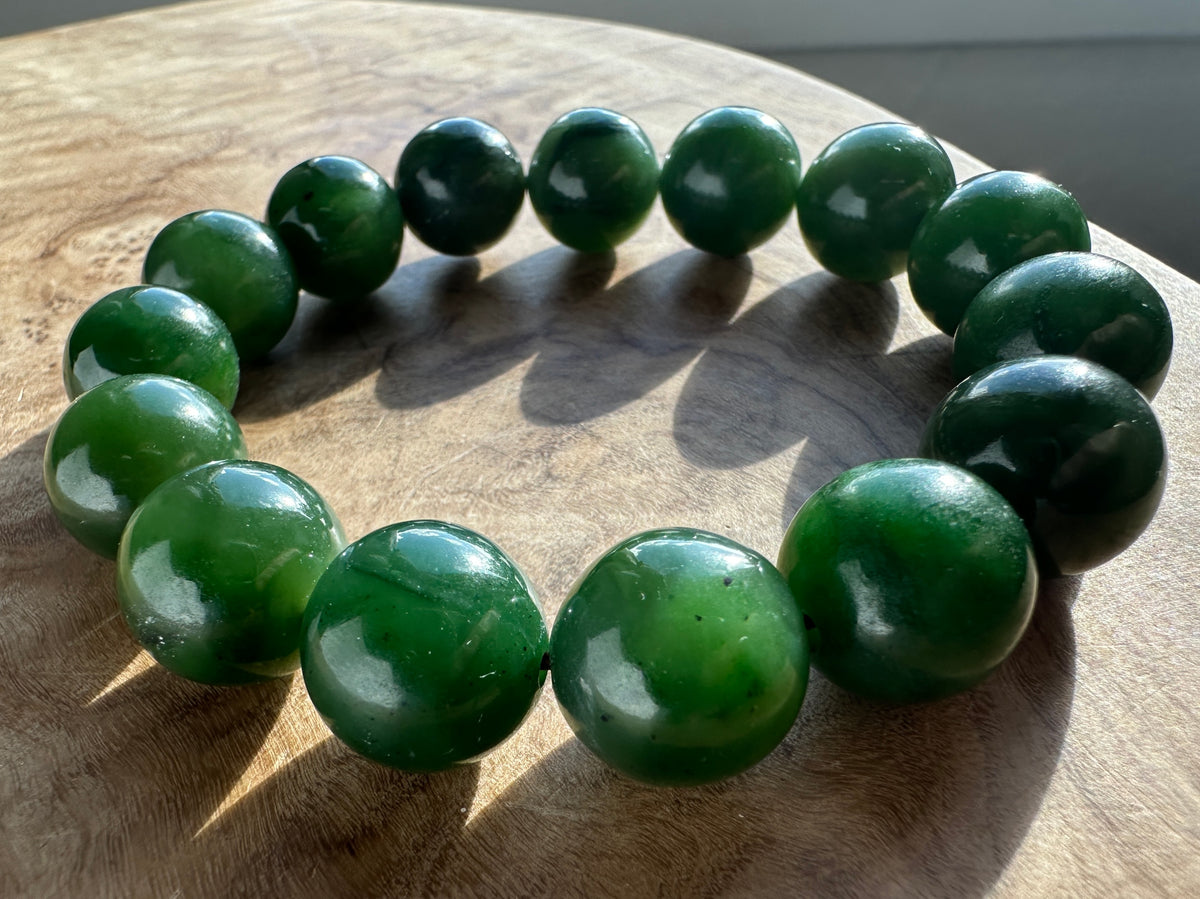 Close up of 14mm nephrite jade beads bracelet held between fingers.