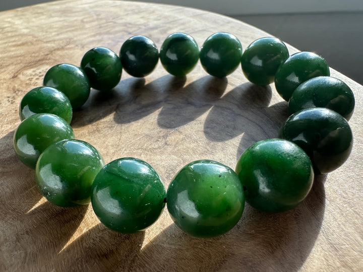 Close up of 14mm nephrite jade beads bracelet held between fingers.
