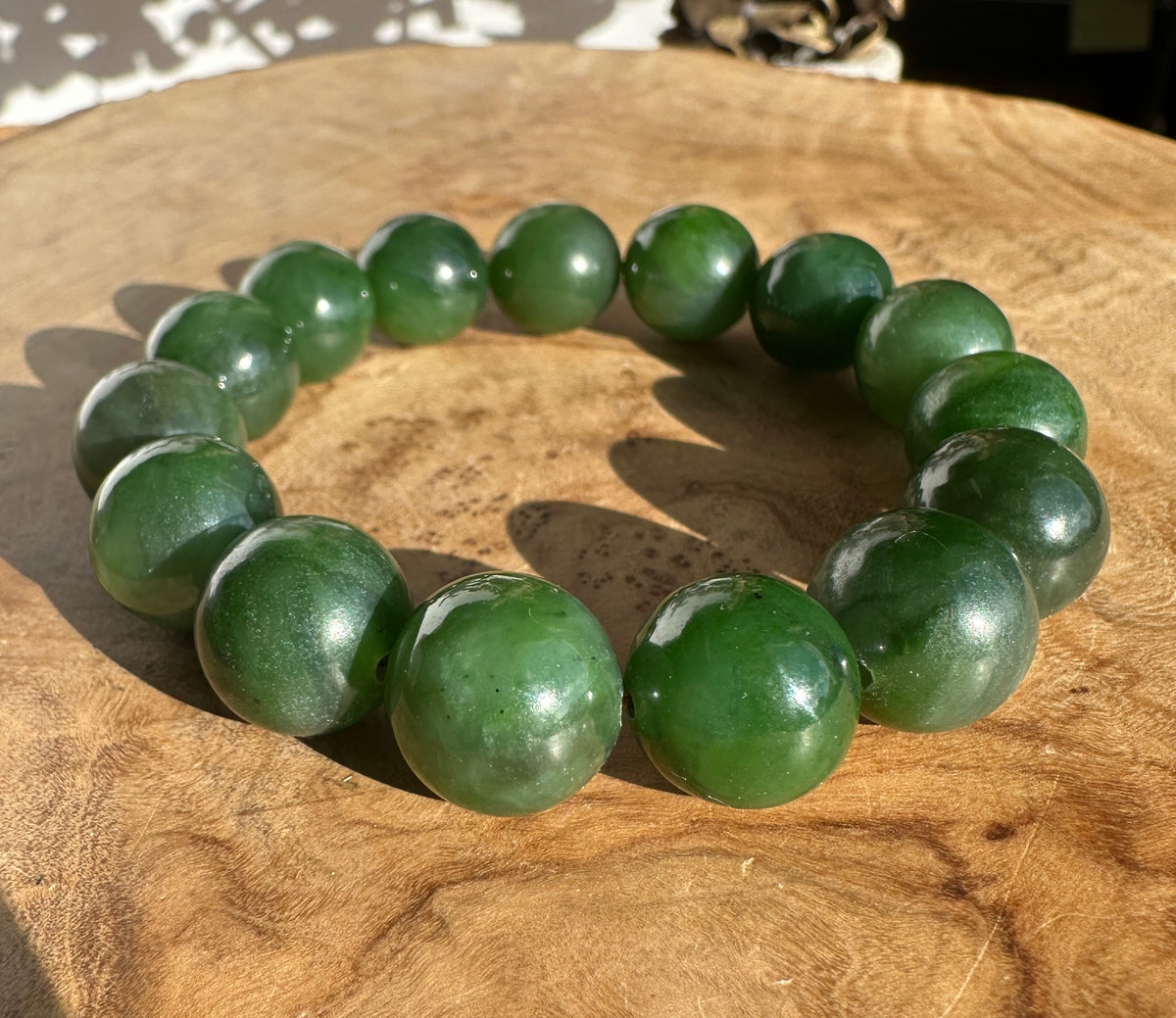Bracelet of 14mm nephrite jade beads arranged in a curve on a wooden surface.