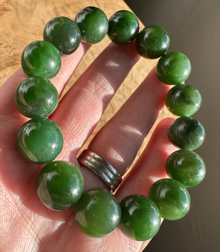 Hand holds a segment of 14mm nephrite jade bead bracelet showing glossy green beads.