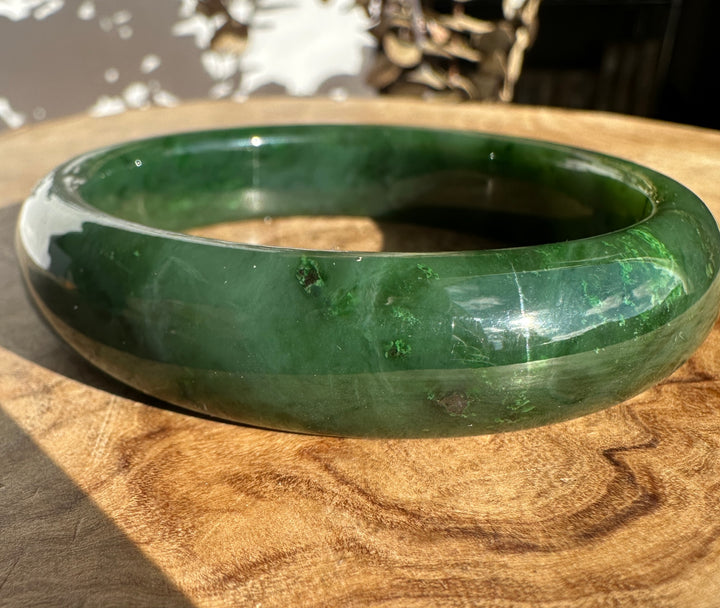 Canadian Jade Bangle 59.8 x 14.5mm in deep green, glossy finish resting on a wooden surface