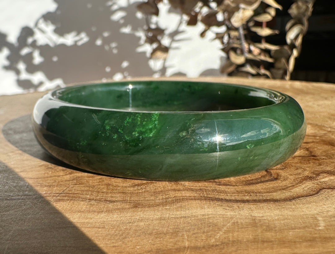 Close up of a green jade bangle resting on a wooden surface