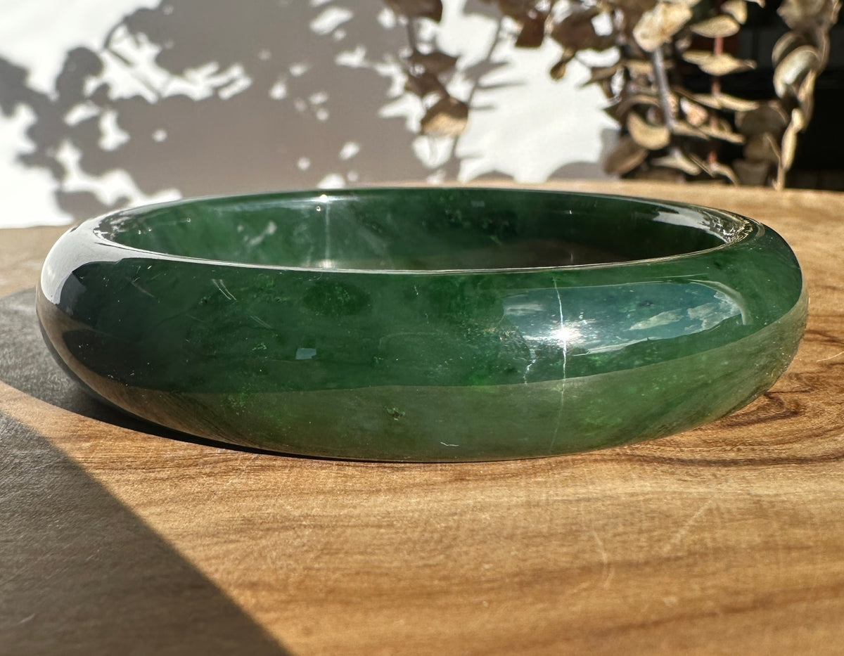 Side view of the Canadian Jade Bangle held between fingers, showing its smooth curved edge