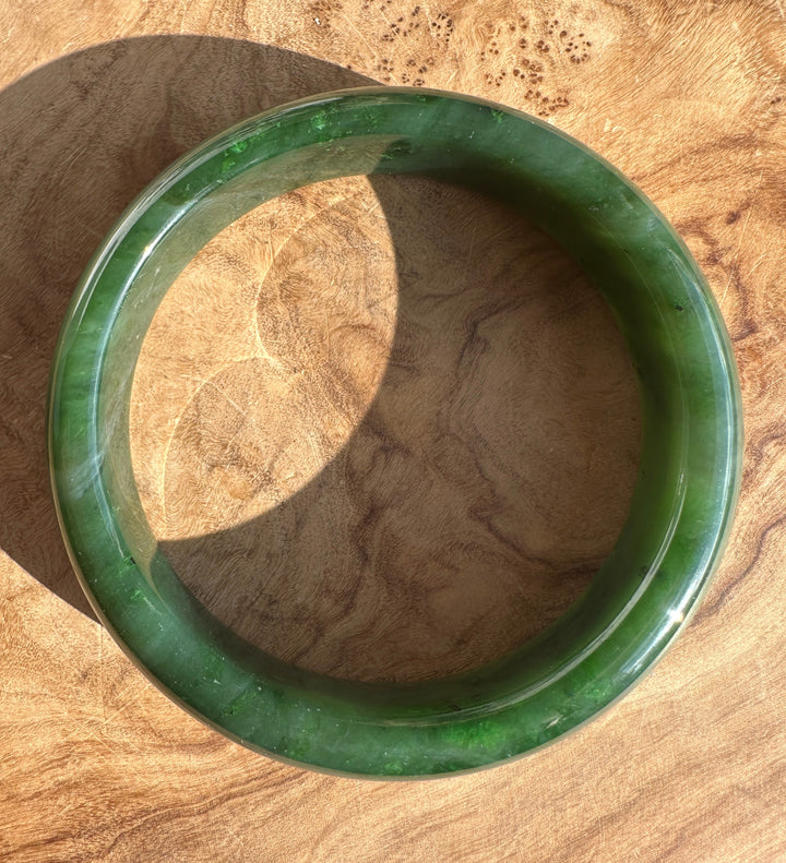 Top-down angle of the Canadian Jade Bangle on wood, highlighting vibrant green with natural pattern.