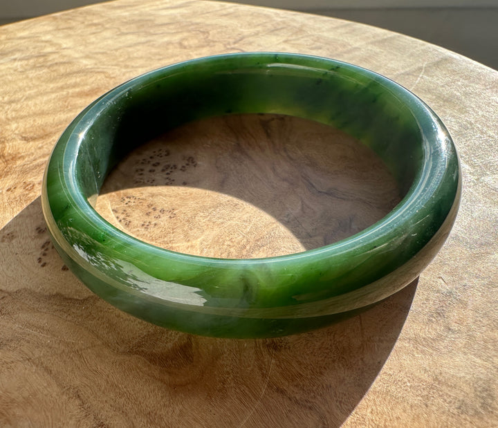 Canadian Jade Bangle 59.8 x 14.5mm on a wooden table, close-up of the glossy green band.