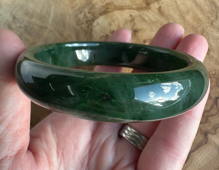 Top view of the green jade bangle being held in hand with a polished surface