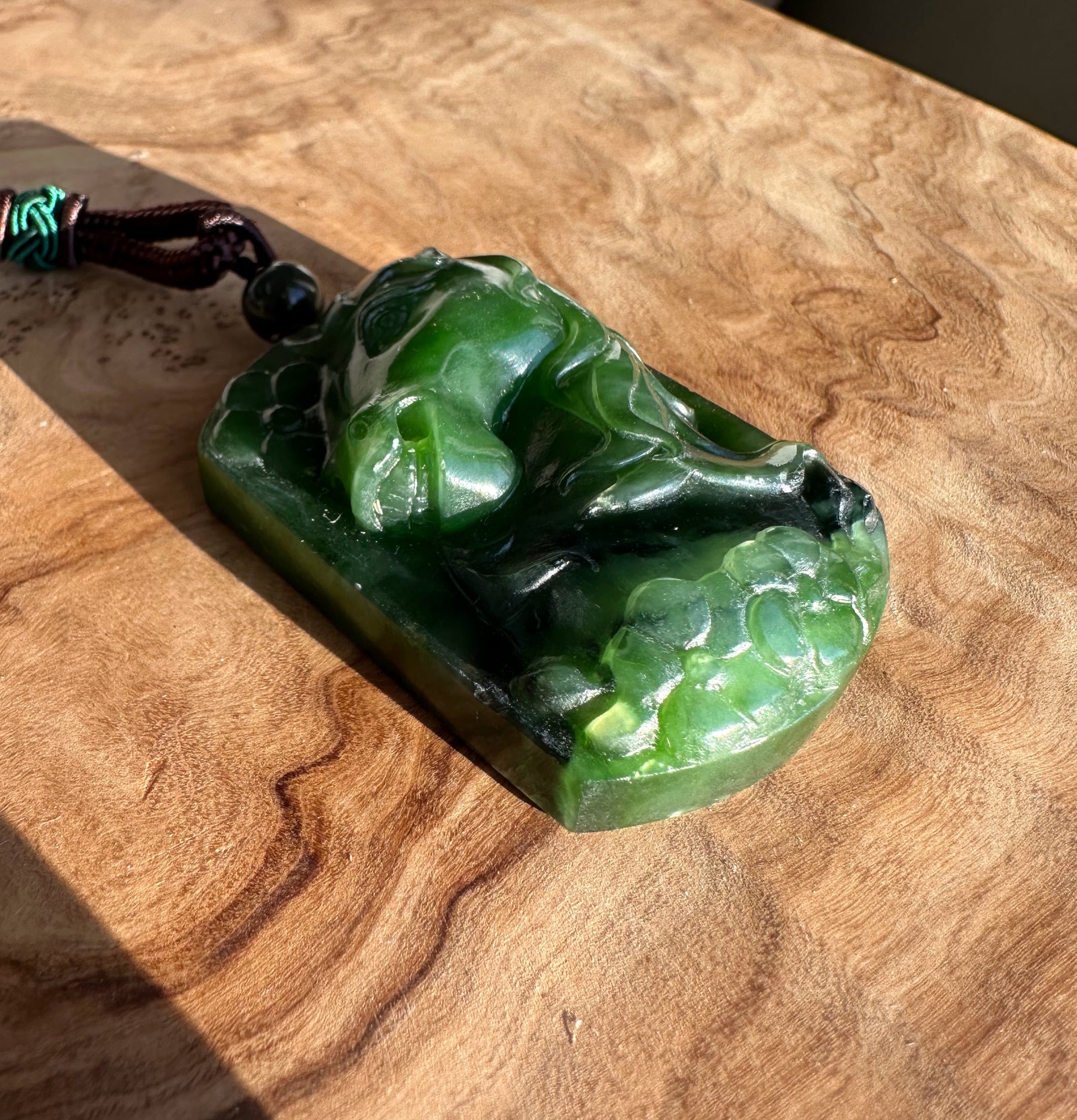 Green jade horse pendant with brown braided cord and bead resting on a wood surface