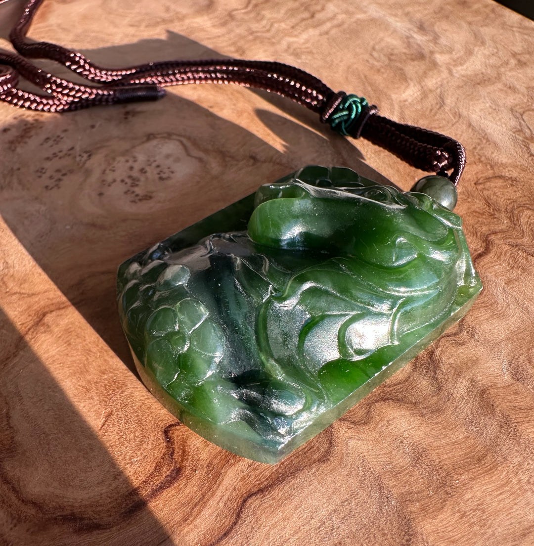 Close-up of green jade horse pendant with flowing carved details and brown braided cord