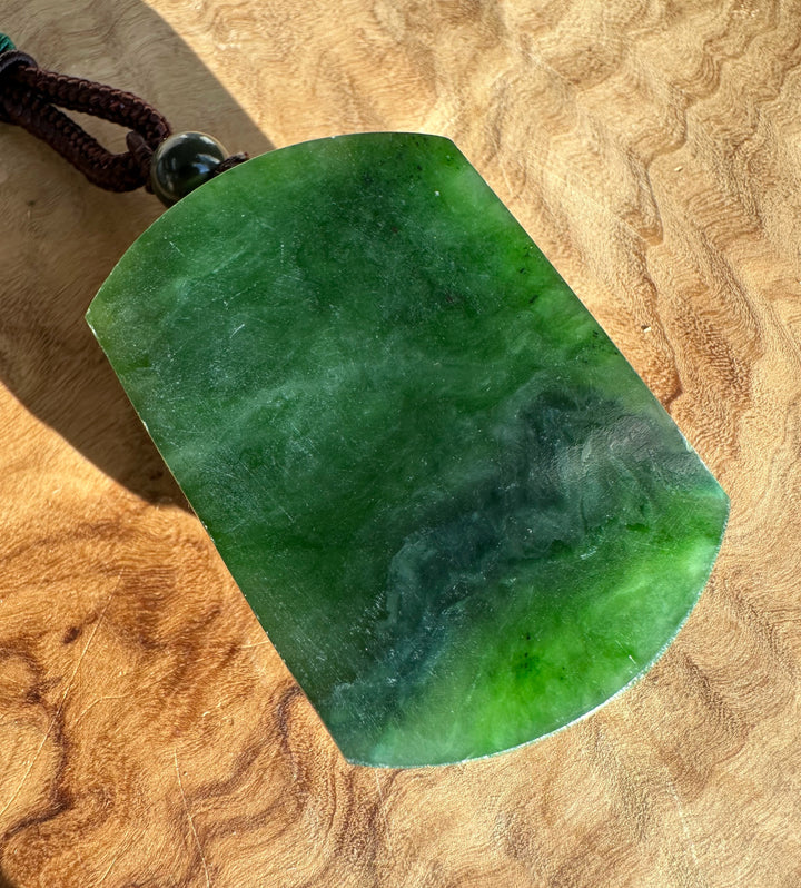 Back view of green jade horse pendant showing smooth surface and attached cord on a wood background