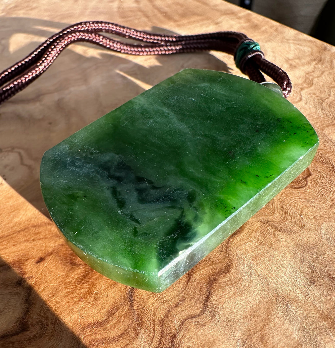 Green jade horse pendant with brown braided cord resting on a wooden surface
