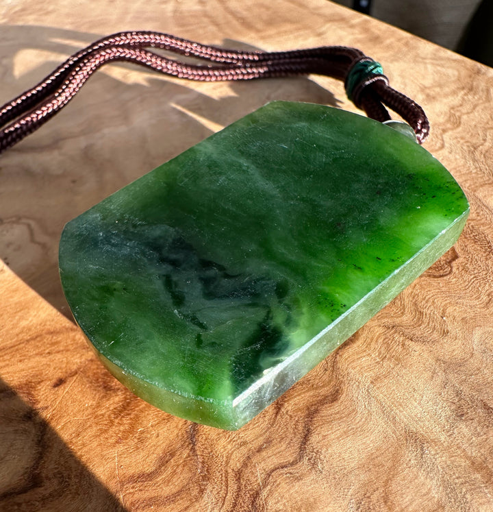 Green jade horse pendant with brown braided cord resting on a wooden surface