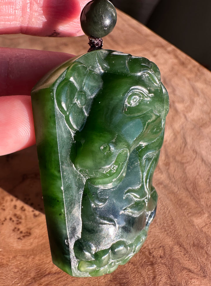 Close-up of green jade horse pendant with carved horse motif and swirls on a cord with a bead