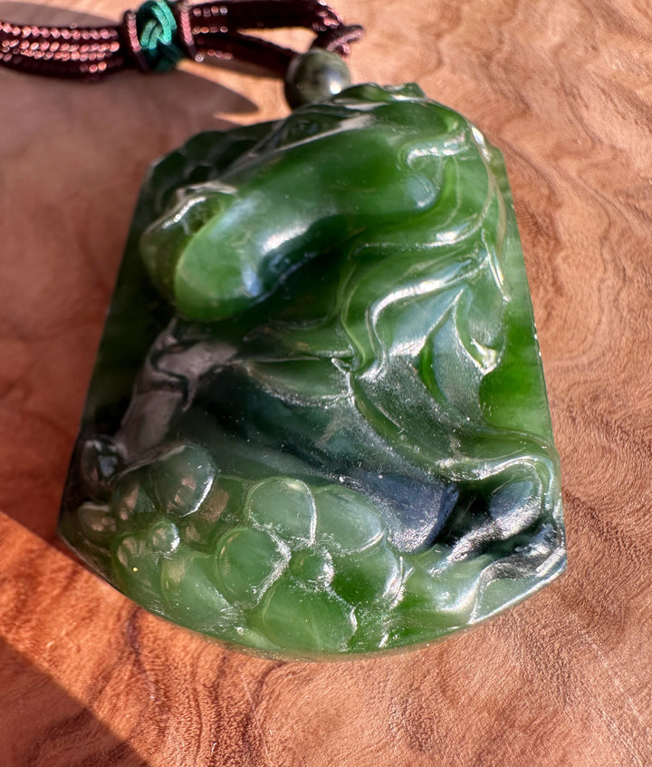Side angle of green jade horse pendant showing carved details and attached cord with bead
