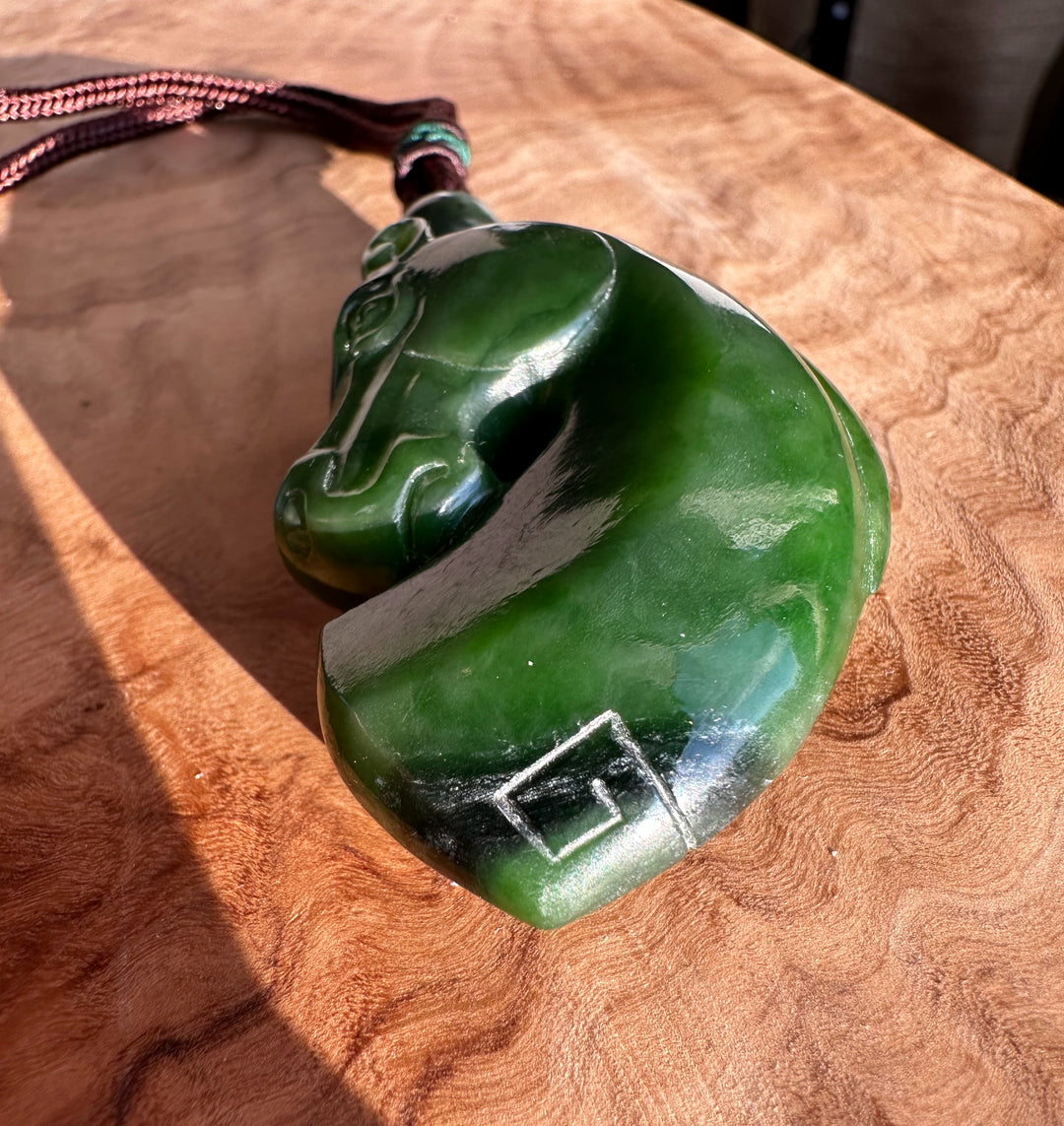Canadian Jade Horse Pendant on a wooden table, side angle highlighting the carved green jade horse head and curved body with cord.