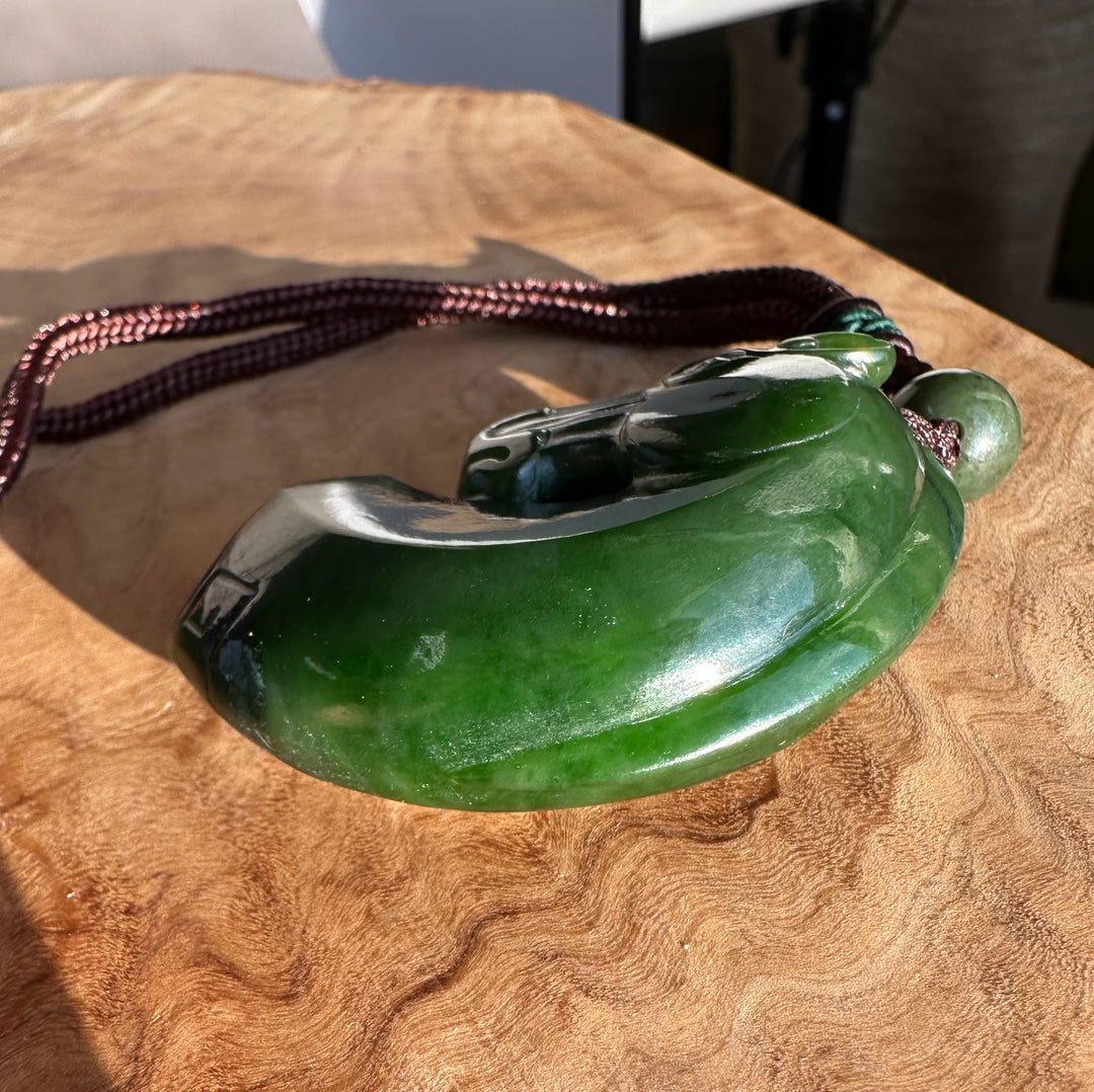 Green jade horse pendant carved from nephrite on a brown braided cord resting on wood