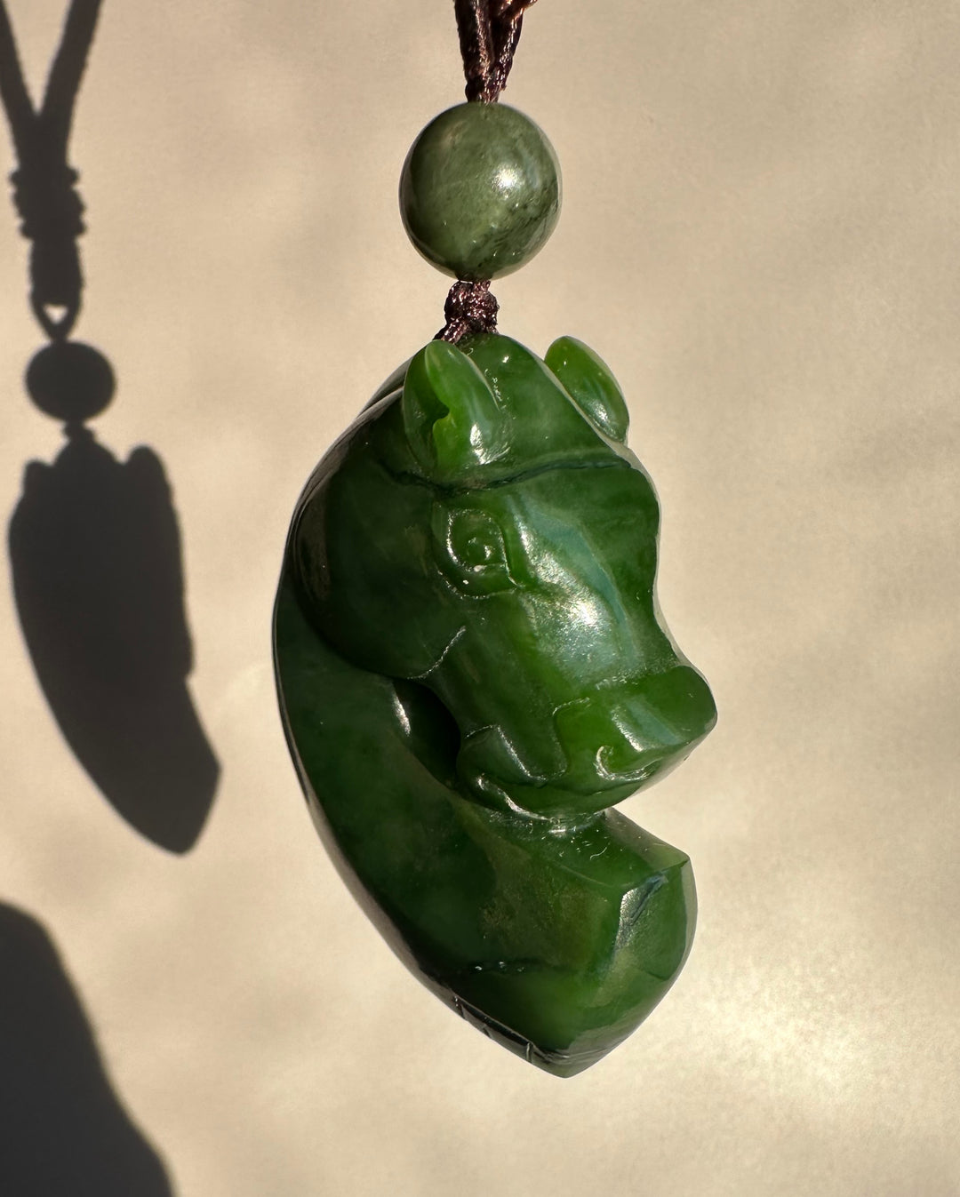 Canadian Jade Horse Pendant featuring a carved green jade horse head suspended by a brown cord with a round bead above.