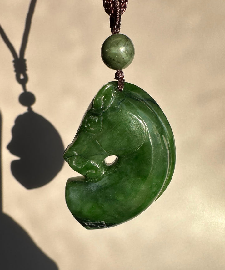 Canadian Jade Horse Pendant carved from green disk with a horse head silhouette, hanging on a brown cord with a round bead.