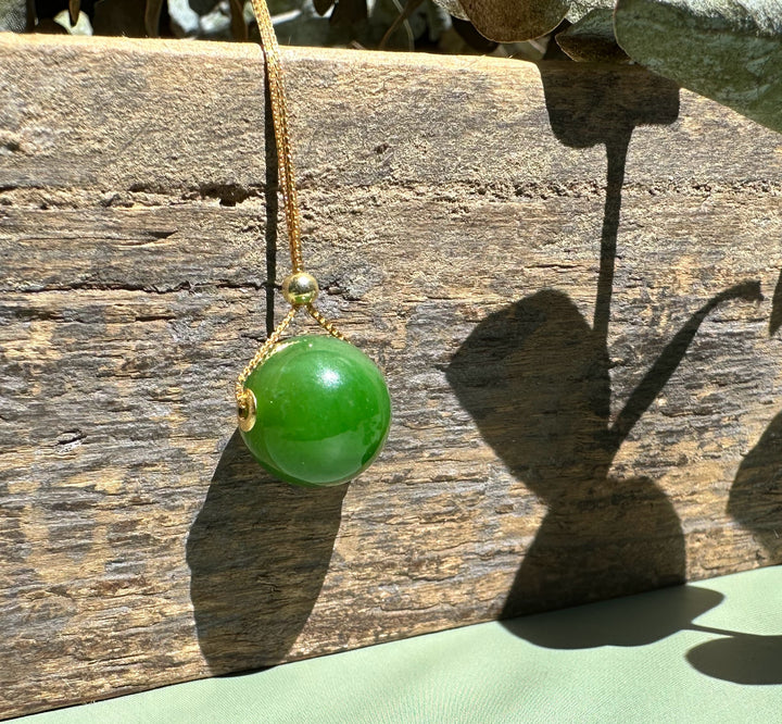 A bright green jade bead pendant with gold bail on a delicate chain against weathered wood